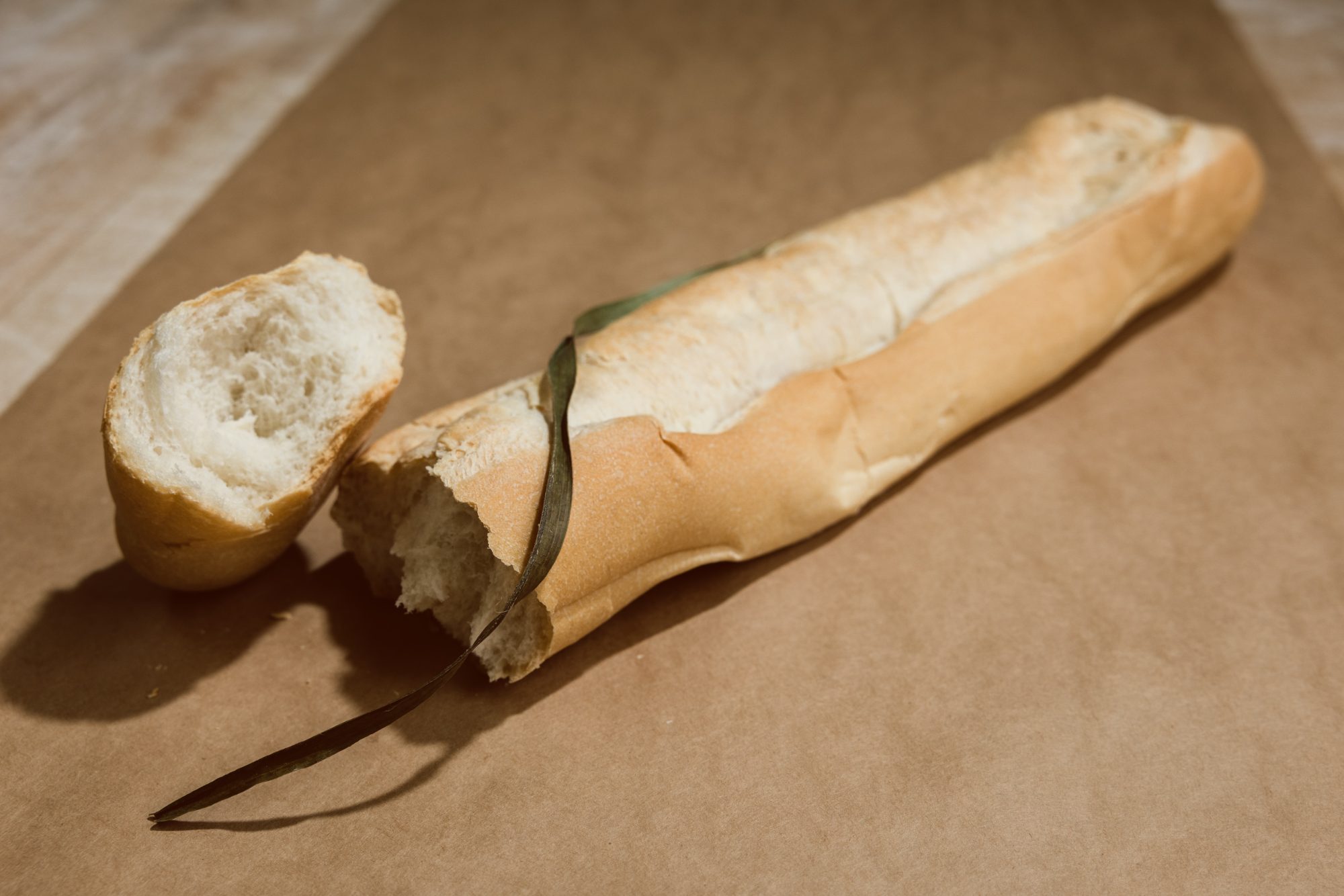 An 18-inch La Segunda Cuban bread loaf on kraft paper with a hand-torn end, the palmetto-leaf split running down its length.