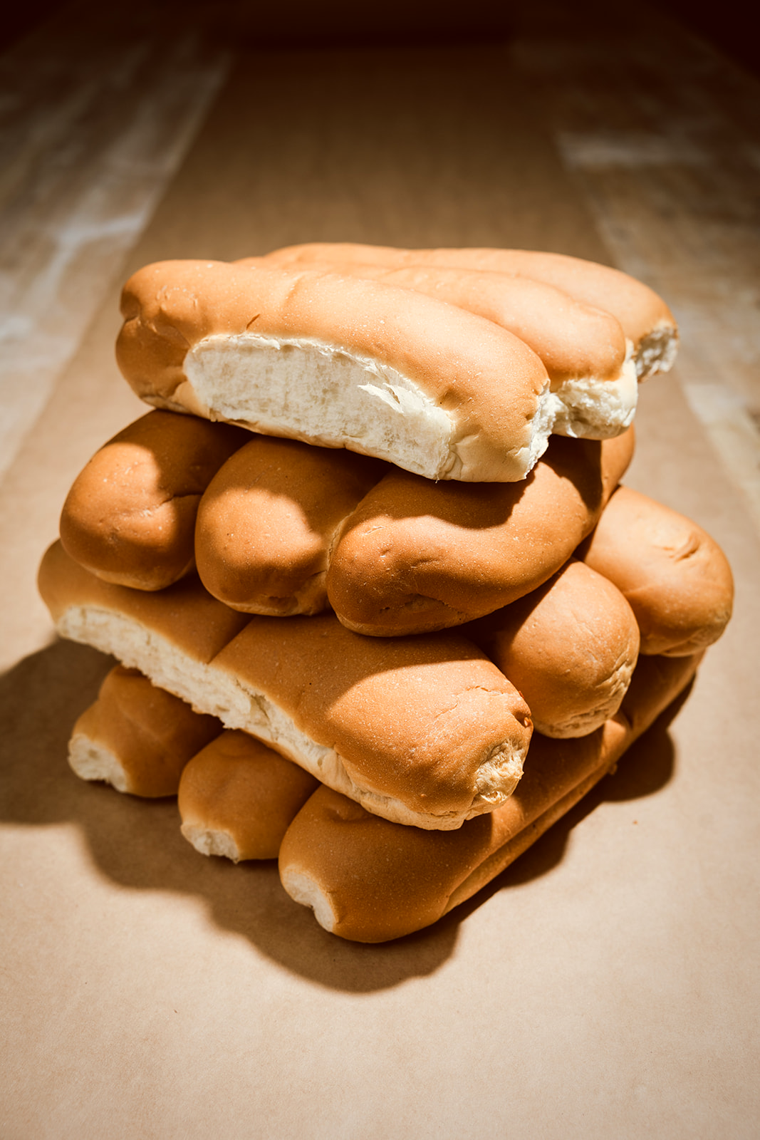 A stack of fresh 8-inch and 12-inch La Segunda hoagie rolls on brown kraft paper in warm morning light, baked that morning for Tampa Bay delivery.